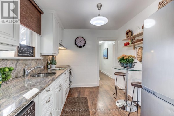 Kitchen with white cabinets, granite countertops, stainless steel refrigerator, and a view down a hallway. - 376 Glen Manor Drive, Toronto