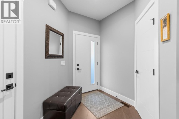 Entryway with light grey walls, dark hardwood floor, white doors, bench, and decorative mirror. - 3763 St. James Drive, West Kelowna