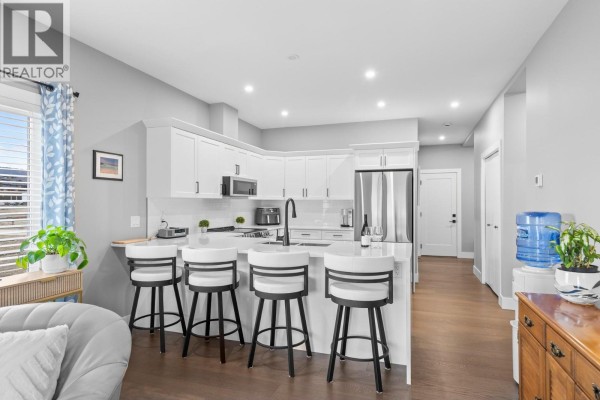 Modern kitchen with white cabinets, grey counters, island with four stools, and stainless steel appliances. - 3763 St. James Drive, West Kelowna