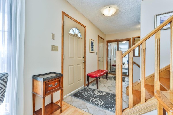 Interior entryway with a beige door, tiled floor, and wooden staircase. - 3764 30 St Nw, Edmonton
