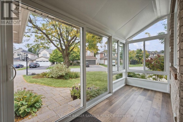 Interior view of a sunroom with large windows, wood-look flooring, and a view of the front yard. - 3766 Mountain Meadows Crescent, Ottawa