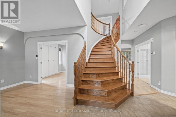Interior view of a two-story foyer with a grand wooden staircase and light grey walls. - 3766 Mountain Meadows Crescent, Ottawa