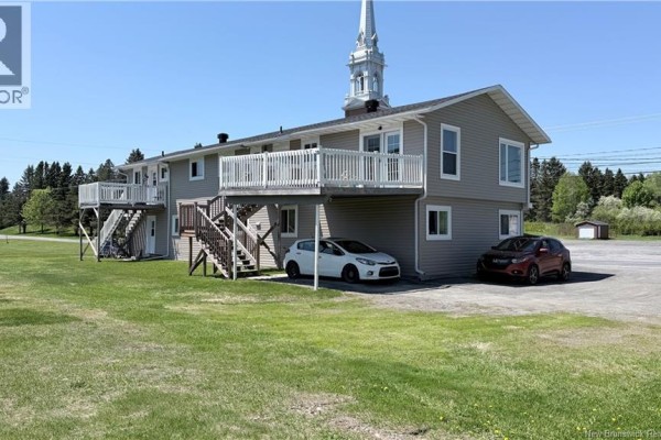 Side and rear exterior of a multi-family building with grey siding, outdoor stairs, and parked cars. - 3766 Principal Street, Baker Brook