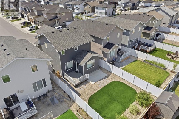 Backyard view of a house with a wooden deck, green lawn, and white vinyl fencing. - 377 Germain Manor, Saskatoon