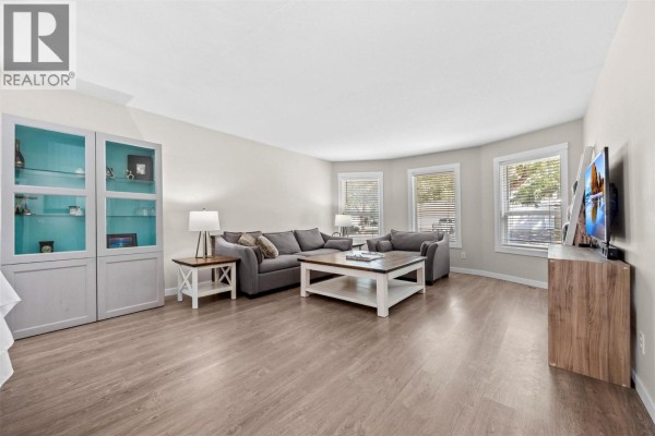 Living room with a large grey sectional sofa, coffee table, and display cabinet with glass doors. - 377 Sumac Road E, Kelowna