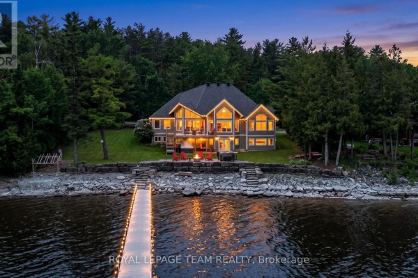 Wooden dock extending into a lake with a blue inflatable raft, leading to a large grey house. - 3778 Armitage Avenue, Ottawa