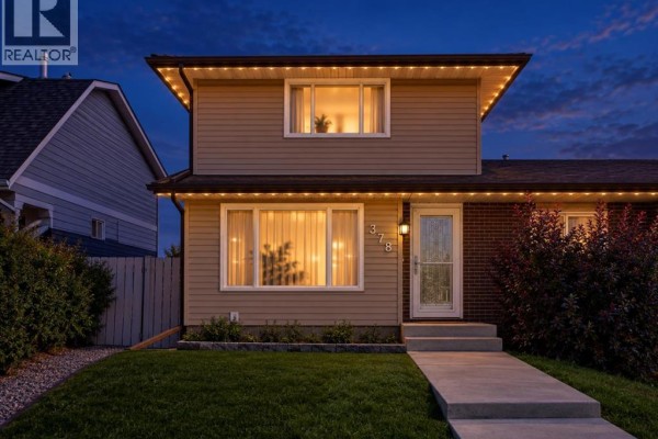 Front exterior of a beige duplex at dusk decorated with string lights. - 378 Midridge Drive Se, Calgary