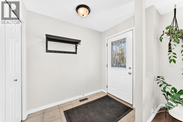 Foyer with a white door, tiled floor, and a black coat rack. - 378 Midridge Drive Se, Calgary