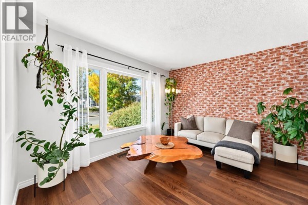 Living room with a large window, a brick accent wall, and a sectional sofa. - 378 Midridge Drive Se, Calgary