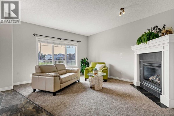 Living room with a fireplace, beige sofa, and view of the staircase and entryway. - 378 Sagewood Gardens Sw, Airdrie