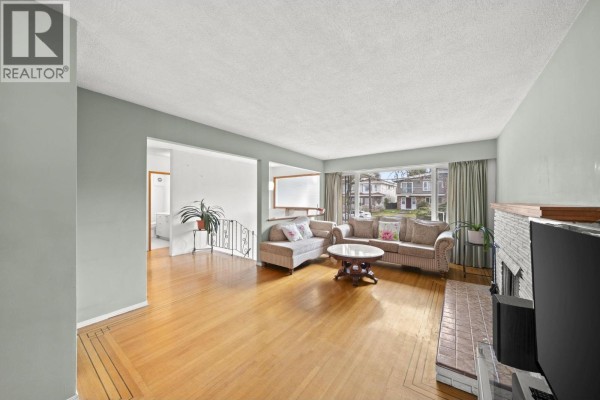 Bright living room with a fireplace, hardwood floors, and a large window view. - 3783 Price Street, Burnaby
