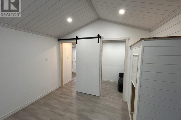 Interior room with white plank ceiling, gray laminate flooring, and white walls, featuring two doorways. - 3786 Prospect Road, Casey Corner