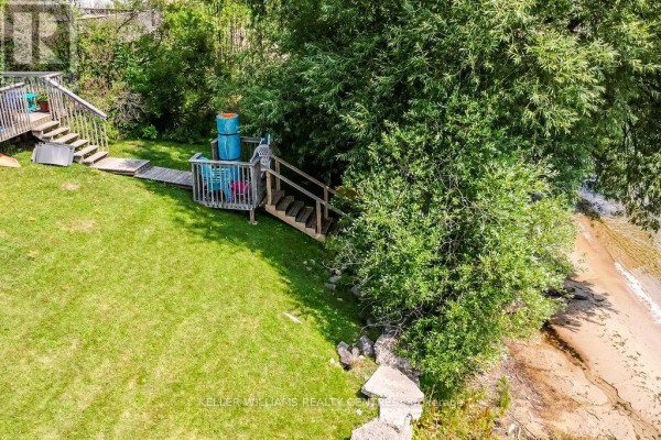 Deck area with stairs leading to the beach, surrounded by grass and trees. - 379 Champlain Road, Penetanguishene