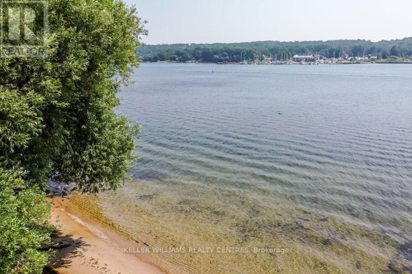 View of the waterfront with sandy beach and calm water, lined by trees. - 379 Champlain Road, Penetanguishene
