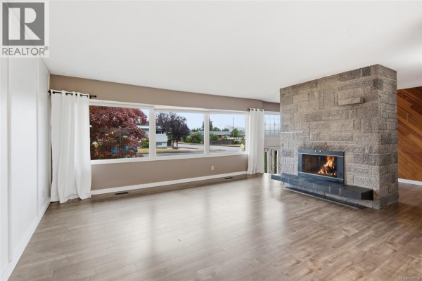 Close-up of a large grey stone fireplace with a black metal insert and tiled hearth. - 3795 Michigan Rd, Port Alberni