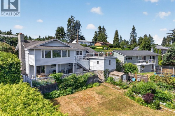 Rear exterior of a light gray house with a sloped lawn, large trees, and multiple decks. - 3798 Laurel Dr, Royston