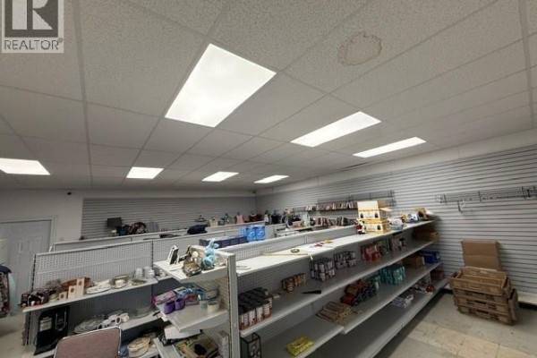 Retail space with multiple white metal shelves displaying merchandise and fluorescent ceiling lights. - 3799 Main Street, Belledune