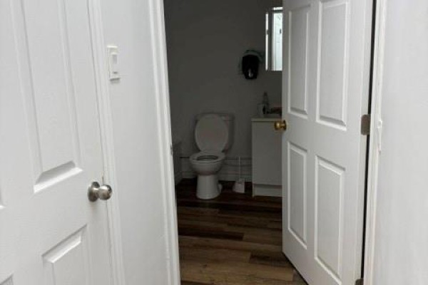 View of a small bathroom with a white toilet and vanity through an open doorway. - 3799 Main Street, Belledune