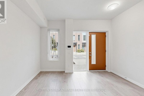 Interior view of an empty room with light wood floors and a front door. - Th 42 - 1020 Portage Parkway, Vaughan