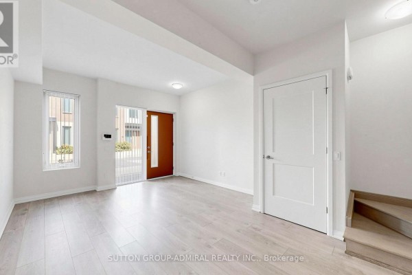 Empty room with light wood floors, white walls, a front door, and a staircase. - Th 42 - 1020 Portage Parkway, Vaughan
