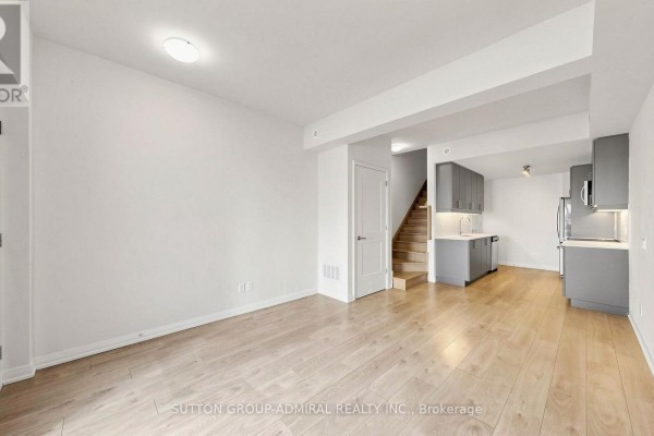 Living area with light wood floors and an open view to a grey kitchen and stairs. - Th 42 - 1020 Portage Parkway, Vaughan