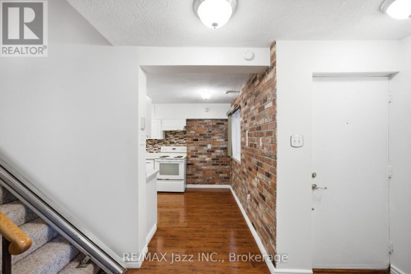 Interior hallway showing stairs, a white door, and entrance to a kitchen with brick accent wall. - 38 - 120 Ling Road, Toronto