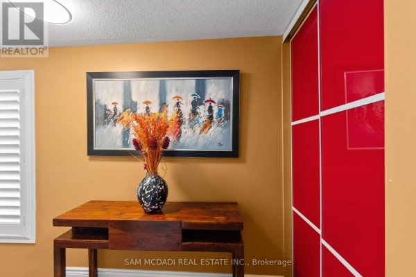 Hallway detail featuring a wooden console table, vase with dried flowers, and a red sliding closet door. - 38 - 6625 Falconer Drive, Mississauga