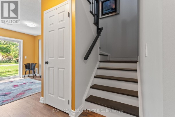 Interior hallway with a white door, wood laminate flooring, and a staircase with dark treads. - 38 - 6625 Falconer Drive, Mississauga