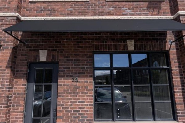 Exterior of brick building with a black awning over a glass door and large window. - 38 - 74 Jutland Road, Toronto