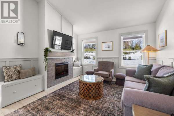 Living room featuring a fireplace, purple sofa, and large windows with scenic views - 38-102 Schoolhouse Lane, Stanley Bridge