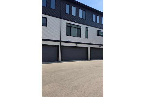 Rear exterior of townhouse with three attached garage doors and dark siding above. - #38 1729 Keene Cr Sw Sw, Edmonton