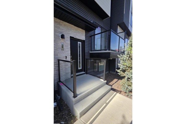 Front entrance steps with concrete, black railings, and glass balcony panels. - #38 1729 Keene Cr Sw Sw, Edmonton