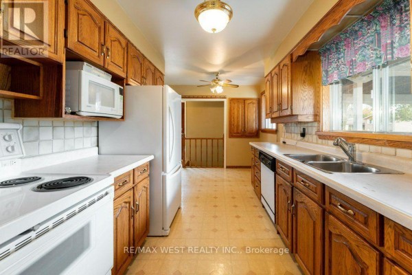 Long kitchen with oak cabinets, white countertops, white appliances, and tiled backsplash. - 38 Albacore Crescent, Toronto