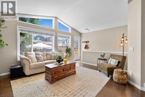 Living room with vaulted ceiling, large windows, beige sofa, wooden coffee table, and dark wood floors. - 38 Auburn Bay Gardens Se, Calgary