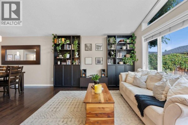 Living room with sofa, wood floors, large windows, and two tall dark bookcases filled with books. - 38 Auburn Bay Gardens Se, Calgary
