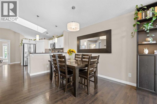 Open concept living and dining room with dark wood floors, large windows, and a dining table for six. - 38 Auburn Bay Gardens Se, Calgary