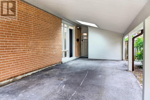View of the covered carport with brick wall and asphalt floor. - 38 Brightside Drive, Toronto