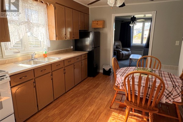 Kitchen area with brown cabinets, a black refrigerator, a sink, and a small dining table with chairs. - 38 Brook Street, Port Aux Basques