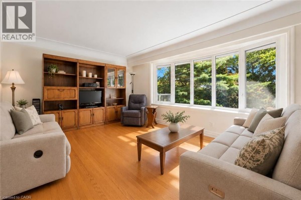 Living room with two sofas, wooden entertainment unit, coffee table, and bay window. - 38 Callander Drive, Guelph