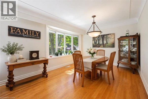 Dining room with oval table, wooden chairs, china cabinet, and bay window view. - 38 Callander Drive, Guelph