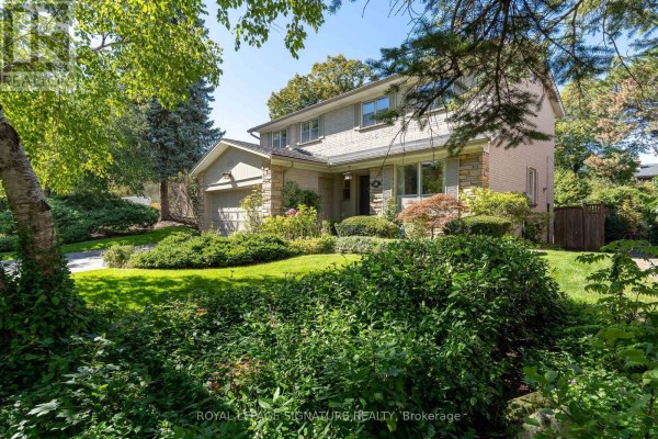 Side view of a brick house with a garage, surrounded by mature trees and lush greenery. - 38 Danville Drive, Toronto