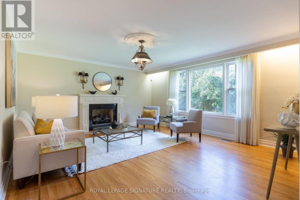 Living room with a white fireplace, sofa, two armchairs, hardwood floors, and a large window. - 38 Danville Drive, Toronto