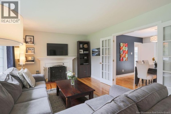Living room with a sectional sofa, fireplace, bookshelf, and view into the dining room. - 38 Forest Road, Rothesay