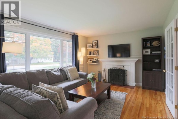 Living room with a large window overlooking the front yard, a sectional sofa, and fireplace with mantel. - 38 Forest Road, Rothesay