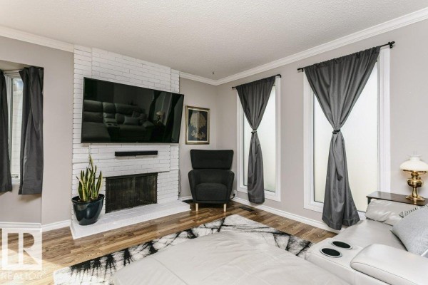 Living room featuring a white brick fireplace with a mounted TV and a black armchair. - 38 Galen Cr, Sherwood Park
