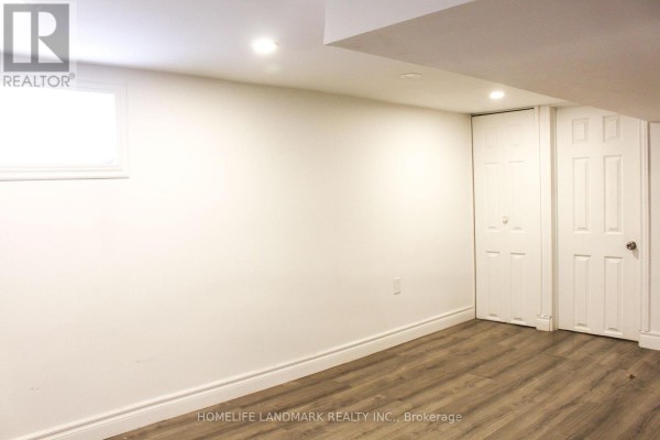Finished basement room with white walls, wood-look laminate flooring, and closed white doors. - 38 Glenvalley Drive, Toronto