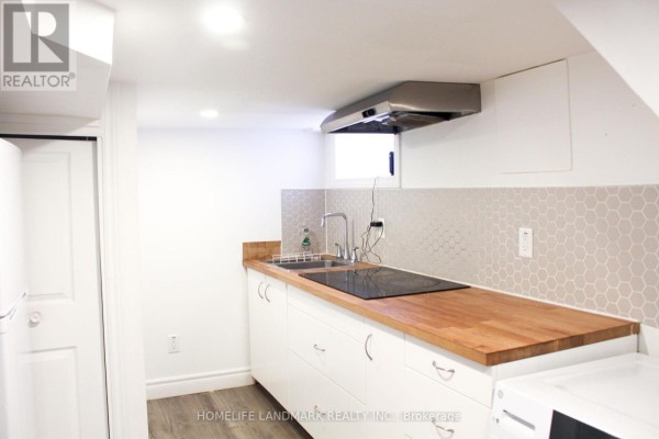 Compact basement kitchen with white cabinetry, wooden countertop, induction cooktop, and hexagonal backsplash. - 38 Glenvalley Drive, Toronto