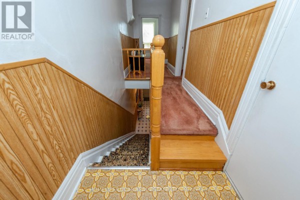 Interior view of a staircase with wood paneling, a red carpet runner, and patterned linoleum flooring. - 38 Gordon Street, Toronto