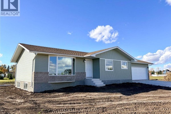 Side view of a light green house with stone accents and a driveway leading to a double garage. - 38 Heritage Cove, Rosthern Rm No  403