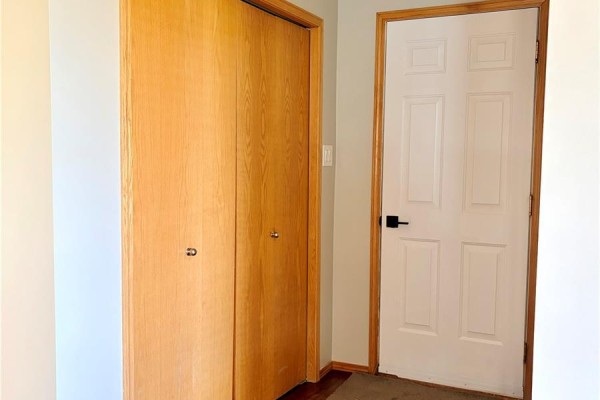 Interior hallway with natural wood bi-fold closet doors and a white paneled door. - 38 Heritage Cove, Rosthern Rm No  403